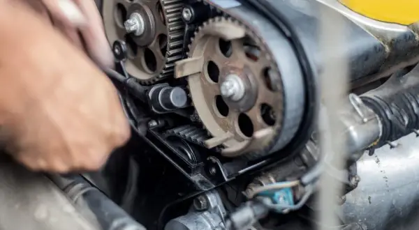 Mano che lavora per cambiare cinghia distribuzione motore auto, con ingranaggi e pulegge in primo piano.