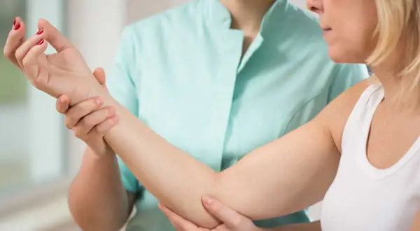Une thérapeute examine le bras d'une patiente, possiblement pour une nevralgie cervico brachiale.