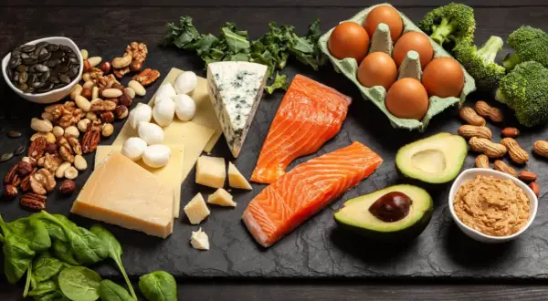 Na talerzu składniki na dietę keto: łosoś, awokado, jajka, sery, orzechy, brokuły i szpinak.