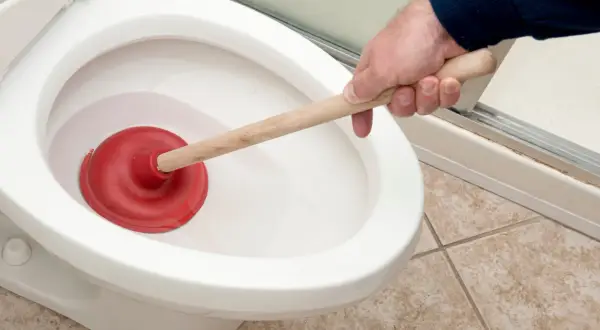 Main tenant utilise une ventouse pour tenter, en vain, de déboucher les toilettes.