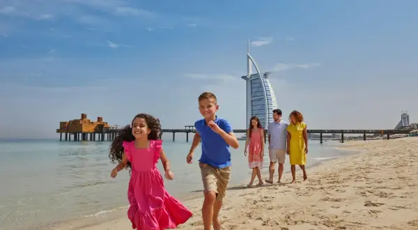 Rodzina bawi się na plaży w Dubaju, z hotelem Burdż al-Arab w tle. Czy w Dubaju jest bezpiecznie? Tak, to idealne miejsce na rodzinne wakacje.