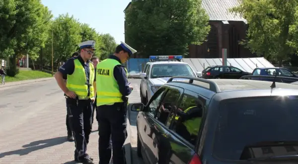 Policjanci wypisują mandat za jazdę po chodniku. Jeden z funkcjonariuszy spisuje dane kierowcy w samochodzie.