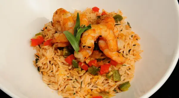 Delicioso arroz con gambas y verduras, con pimientos rojos y verdes, y una hoja verde decorativa.