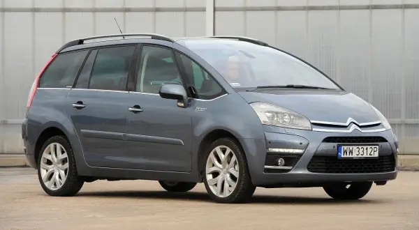 Szary Citroen C4 Grand Picasso 2.0 HDI z kierowcą za kierownicą, zaparkowany przed budynkiem.