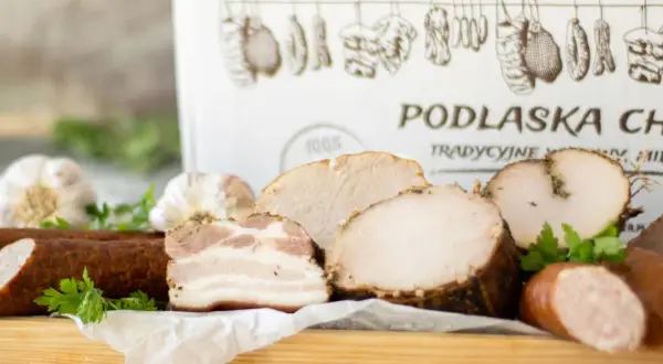 Swojskie wyroby wędliniarskie z Podlaskiej Chaty: kiełbasa, boczek, pieczone mięsa i czosnek. Tradycyjne smaki.