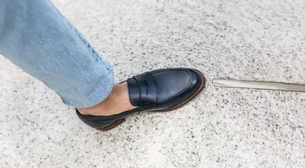 Un homme en jean bleu porte une chaussure de ville marine. L'outil à côté suggère une envie de ressemeler chaussures.