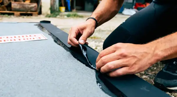 Mains habiles en train d'enlever la colle néoprène d'une bande noire sur une surface grise.