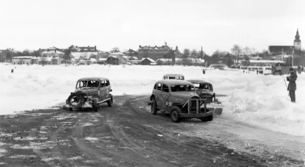 Snöig vinterdag med flera 70 tals bilar redo för race. En åskådare står vid sidan av banan.