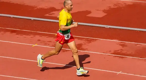 Un athlète en tenue jaune et rouge court sur une piste mouillée, visant le record du monde de vitesse à pied.