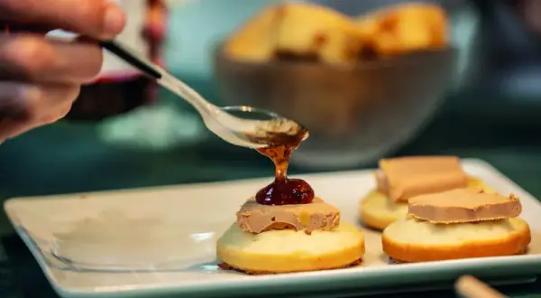 Une cuillère verse une touche de confiture sur un toast original de foie gras. Délicieux !