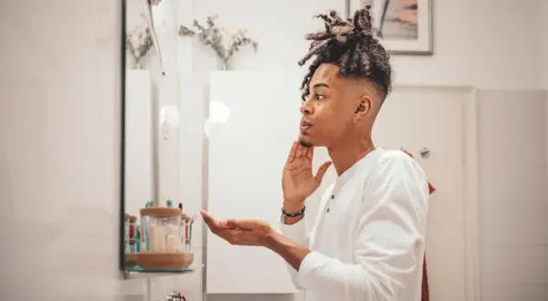 Mann mit Dreadlocks im Spiegel, der sich die Haut richtig reinigen möchte.
