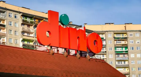 Duże czerwone litery z napisem "dino" na tle bloków mieszkalnych.