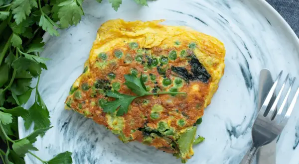 Une omelette aux petits pois et brocolis, garnie de persil frais. Une recette simple et savoureuse pour un repas léger.