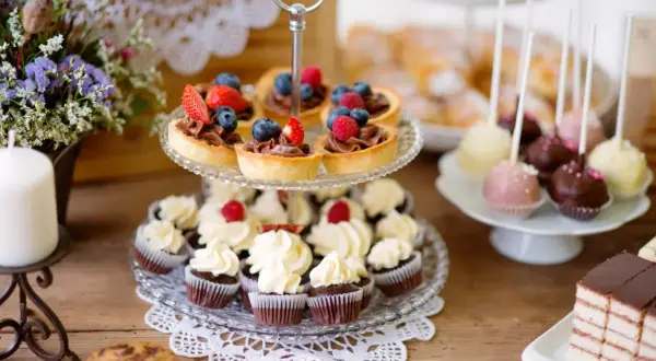 Stół z babeczkami, tartaletkami z owocami, cake pops i ciastem.