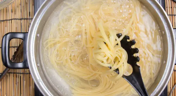 Spaghetti kochen in sprudelndem Wasser. Ein schwarzer Pastalöffel hebt eine Portion heraus, um zu zeigen, wie kleben spaghetti nach dem kochen nicht zusammen.