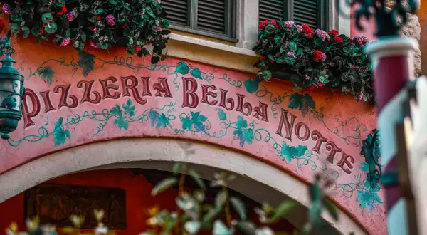 Różowa fasada Pizzerii Bella Notte ozdobiona winoroślą i kwiatami.