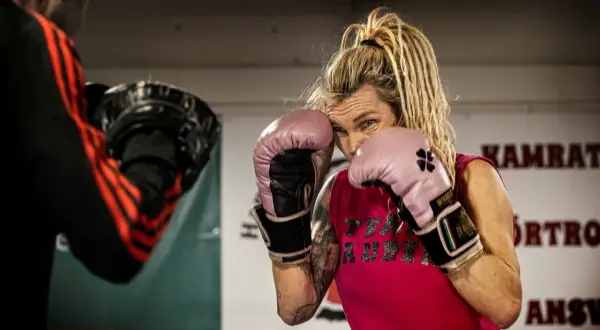 Mikaela boxare i rosa handskar, redo för träning. Hennes blick är fokuserad, med dreadlocks som ramar in ansiktet.
