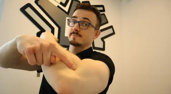 Mężczyzna w okularach wskazuje palcem na zewnętrzną stronę łokcia.