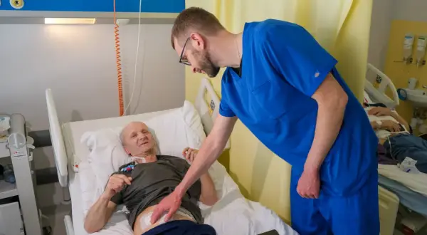 Lekarz pochyla się nad pacjentem w łóżku szpitalnym, omawiając jego rokowania po usunięciu trzustki.