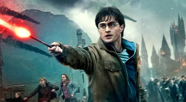 Harry Potter z różdżką w dłoni, w tle bitwa o Hogwart. To scena z serii filmowej Harry Potter.