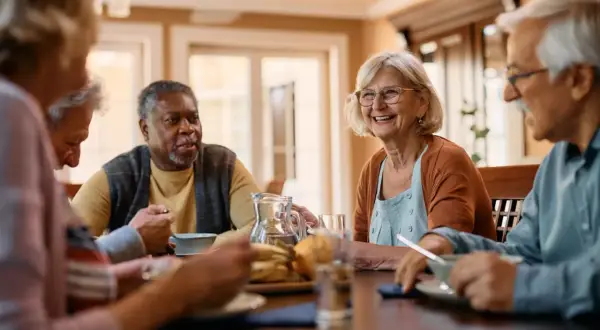 Des seniors joyeux partagent un repas, discutant de ce qu'est un cap retraite.