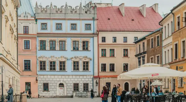 Kolorowe kamienice na rynku, idealne na tani wypad na weekend w Polsce. Ludzie spacerują i siedzą w ogródku kawiarnianym.