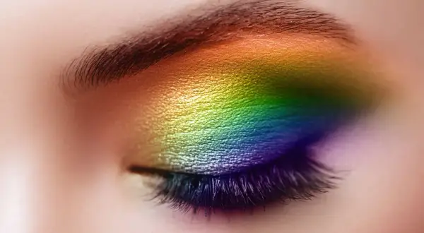 Un œil fermé orné d'un maquillage arc-en-ciel vibrant, du jaune au violet, sublimant le regard. Un maquillage yeux bleus audacieux et coloré.