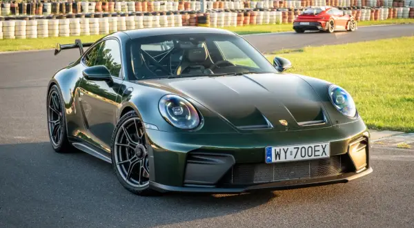 Zielony Porsche 911 GT3 na torze wyścigowym, z innym czerwonym samochodem w tle.