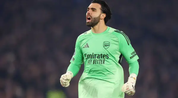 Bramkarz Arsenalu w zielonej koszulce z napisem "Emirates Fly Better", zaciśniętą pięścią i okrzykiem radości.