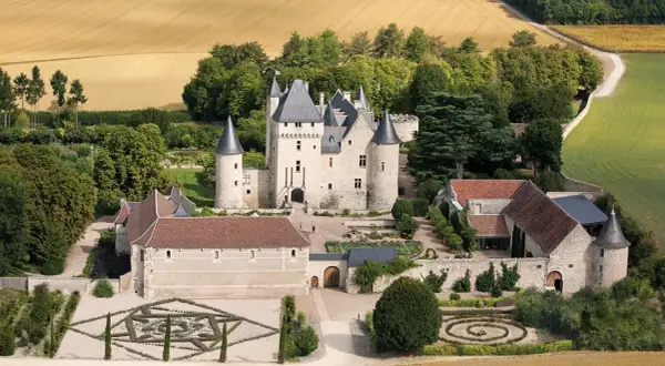 Vue aérienne du **château du Riveau**, un édifice médiéval entouré de jardins à la française et de champs dorés.