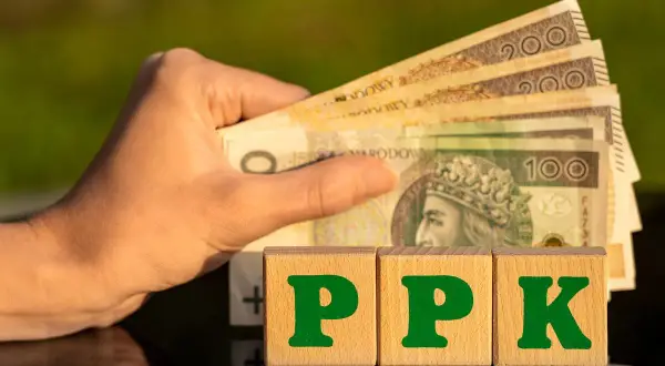 Dłoń trzyma polskie banknoty. Obok kostki z literami PPK. Co to PPK? To przyszłość Twoich oszczędności.