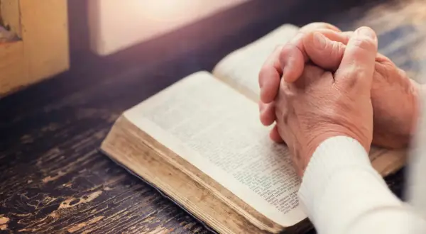 Dłonie złożone nad otwartą księgą, której strony zawierają tekst apostolski.