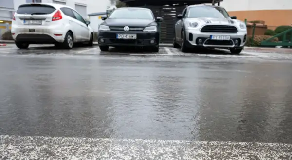 Trzy samochody zaparkowane na mokrym, błyszczącym od lodu asfalcie.