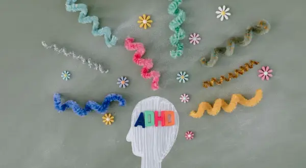 Kolorowe litery "ADHD" w głowie symbolizują diagnozę. Wirujące wstążki i kwiatki odzwierciedlają natłok myśli.