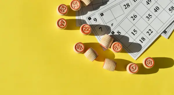 Drewniane krążki z numerami i karty do gry w bingo leżą na żółtym tle, gotowe do emocjonujących konkursów i loterii.