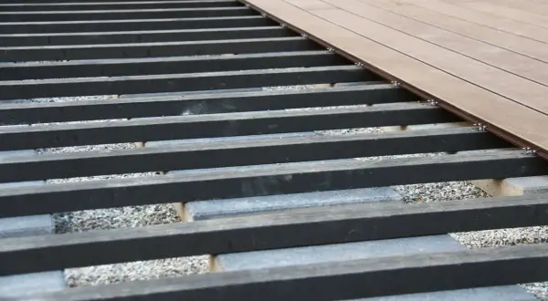 Unterkonstruktion für eine WPC-Terrasse mit grauen Betonsteinen und dunklen Balken, bereit für die Verlegung der braunen Dielen.