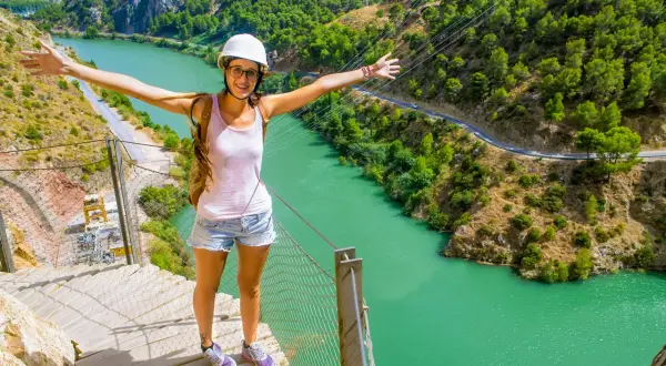 Glad kvinna med armarna utsträckta njuter av en fantastisk caminito del rey vandring med turkos flod nedanför.