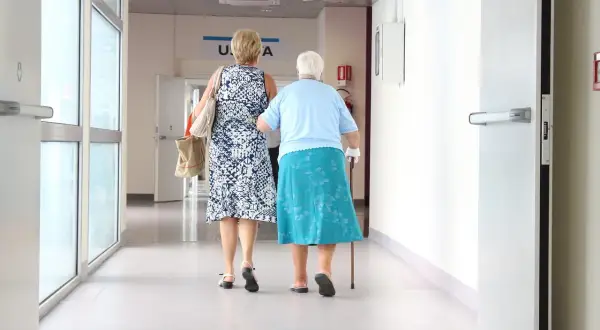 Dwie kobiety idą korytarzem szpitalnym. Jedna wspiera się laską. Być może zmierzają po świadczenia 500 plus dla chorych na raka ZUS.