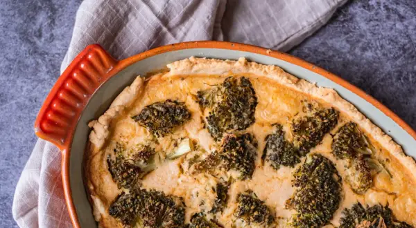 En gyllene ost och broccolipaj i en orange kantig form, redo att serveras.