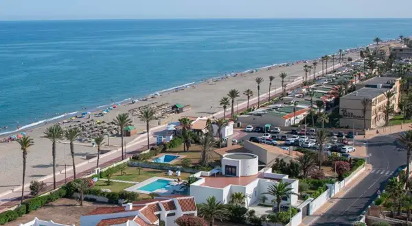 Vista aérea de la playa de las salinas, con gente disfrutando del sol y el mar, palmeras y edificios turísticos.