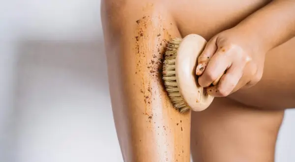 Mano che applica fango dimagrante con spazzola su gamba. Esfoliazione e benessere per la pelle.