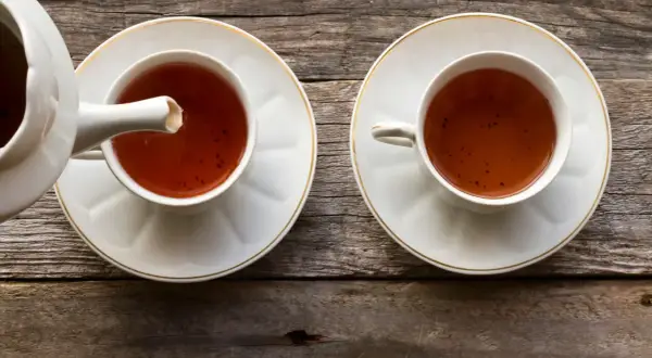 Dwie filiżanki z herbatą pu erh, z których jedna jest nalewana z czajniczka. Napój ma głęboki, bursztynowy kolor, a jego właściwości zdrowotne są cenione od wieków.