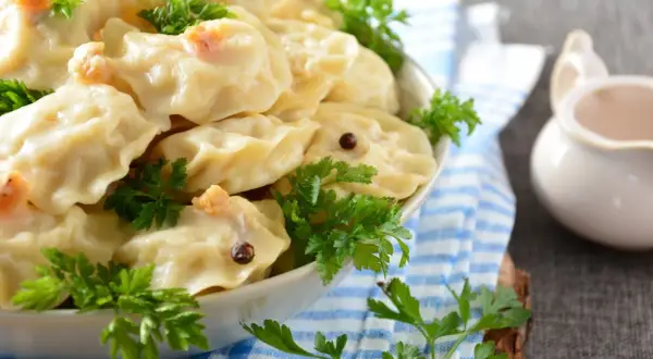 Pyszne pierogi z ziemniakami, udekorowane natką pietruszki i ziarnami pieprzu, czekają na talerzu.