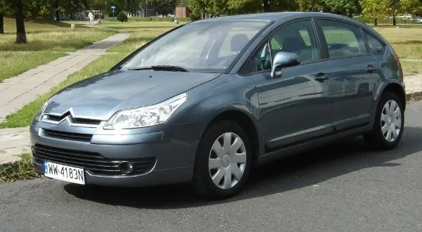 Szary Citroen C4 1.6 HDI zaparkowany przy chodniku w parku.