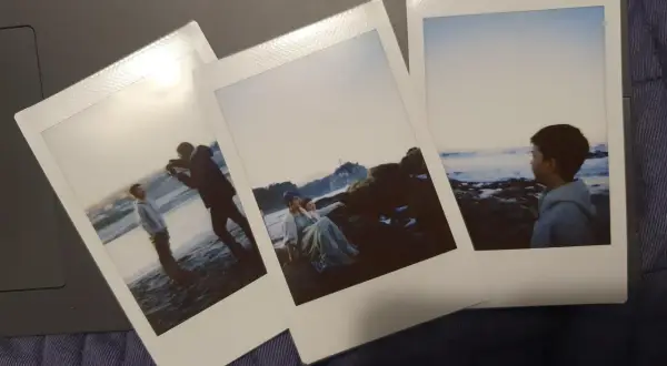 Zdjęcia z Instax pokazują, jak robić zdjęcia na plaży: chłopak fotografuje drugiego, para siedzi na skałach, a trzeci chłopiec patrzy na morze.