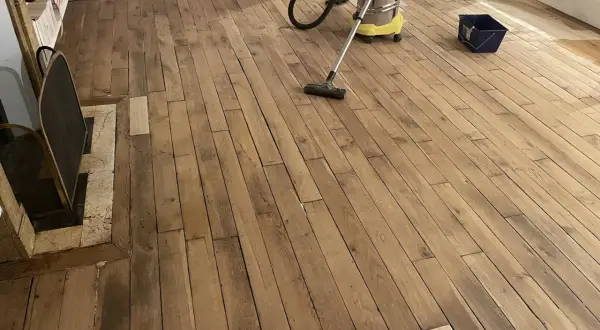 Un aspirateur nettoie un parquet en bois vitrifié, prêt pour une nouvelle couche de protection.