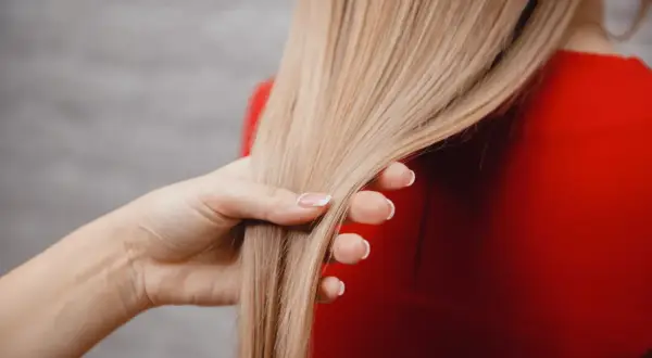 Dłoń dotyka gładkich, blond włosów. To efekt zastosowania tonera do włosów, który odświeża kolor i nadaje blask.
