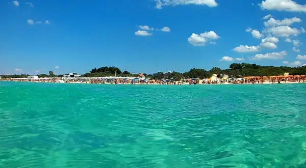 Acque cristalline e una spiaggia affollata a Porto Cesareo, con ombrelloni colorati e gente che si gode il sole. Lu specchia Porto Cesareo, un paradiso estivo.