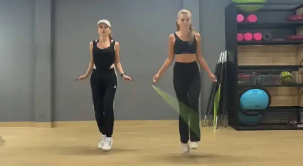 Dwie kobiety w strojach sportowych skaczą na skakance w sali gimnastycznej.
