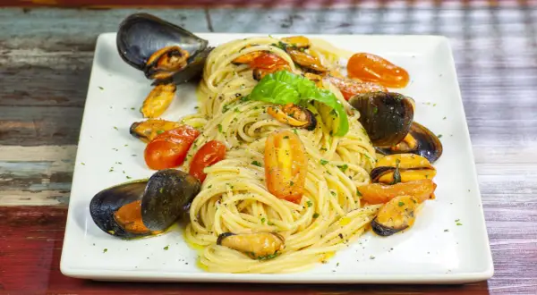 Un piatto invitante di spaghetti con le cozze e pomodorini, guarnito con basilico fresco.